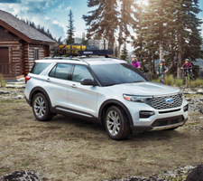 A white explorer parked at a campsite next to three people riding bicycles.